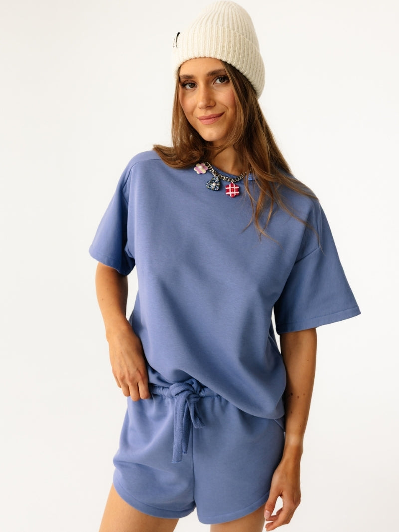Stylowe niebieskie szorty Coast z elastyczną talią i wiązaniem - idealne na letnie dni w odcieniu Timeless Blue. Stylizacja z koszulką od kompletu i kremową czapką.